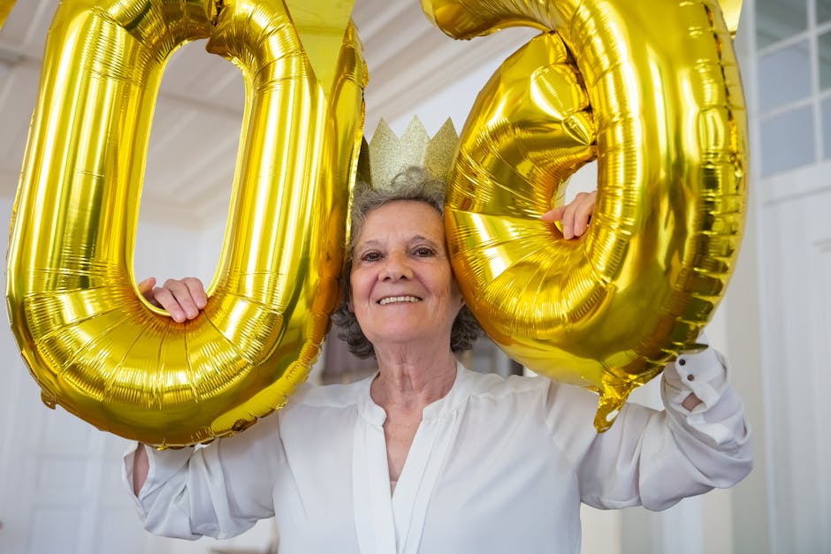 Elderly woman smiles joyfully while holding golden '90' balloons during a birthday celebration indoors
